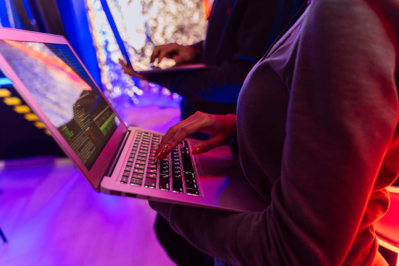 Services-01 Two professionals analyzing data on laptops with colorful lighting, focusing on cybersecurity details.